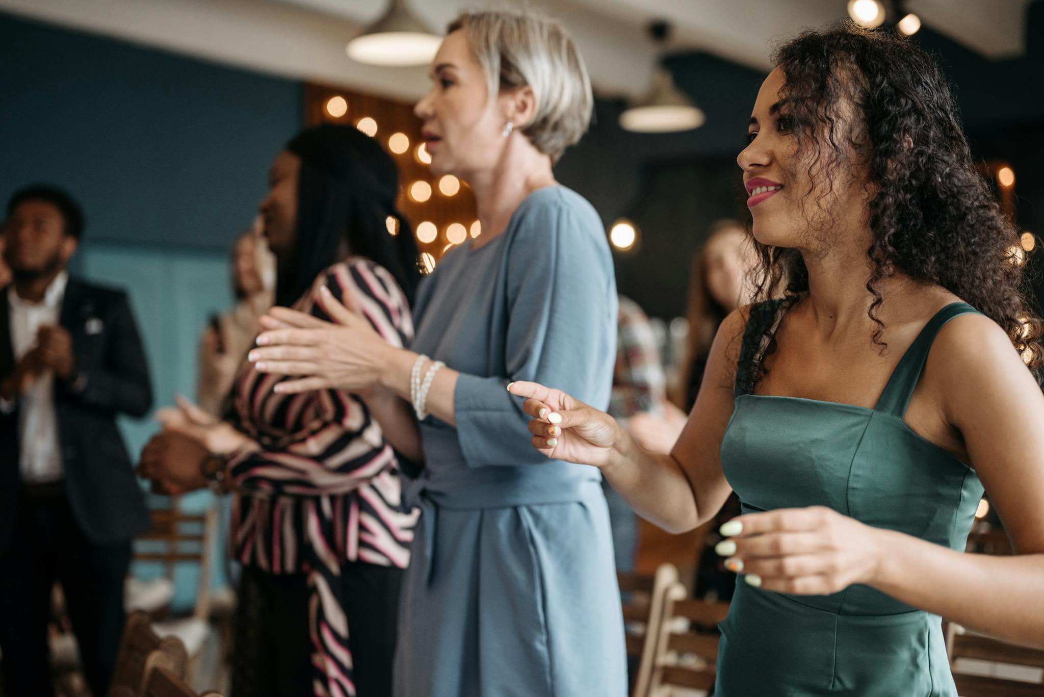 A diverse group of people clapping and standing together at an indoor event.